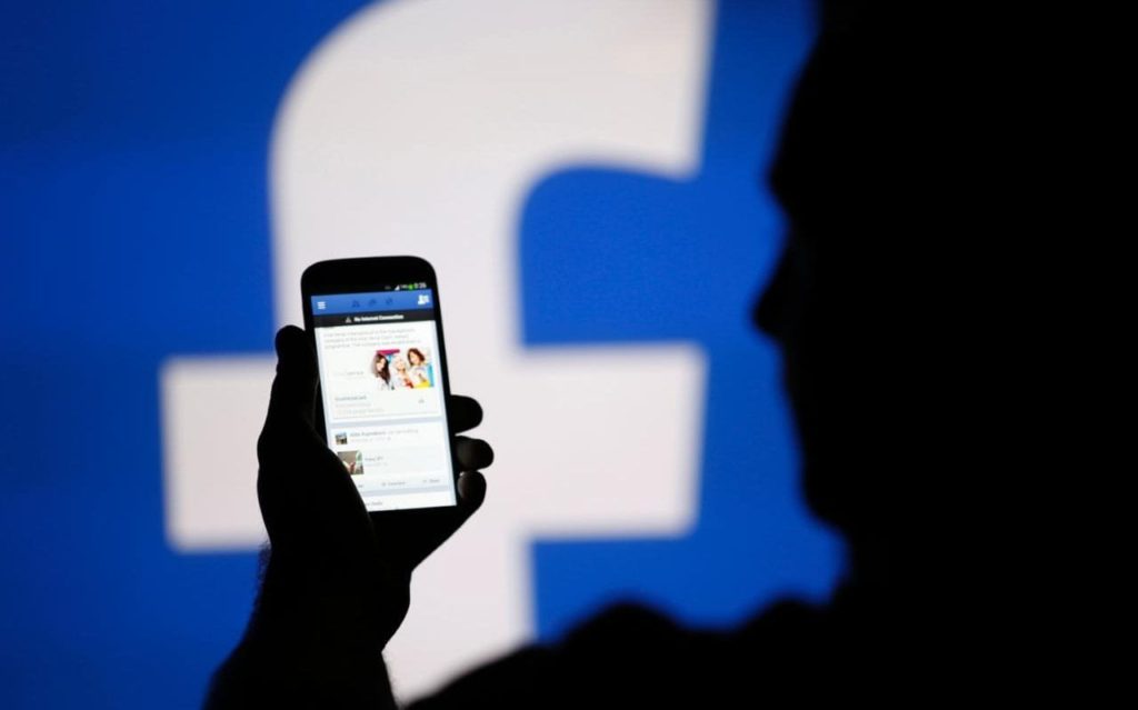 man holding phone with facebook in the background